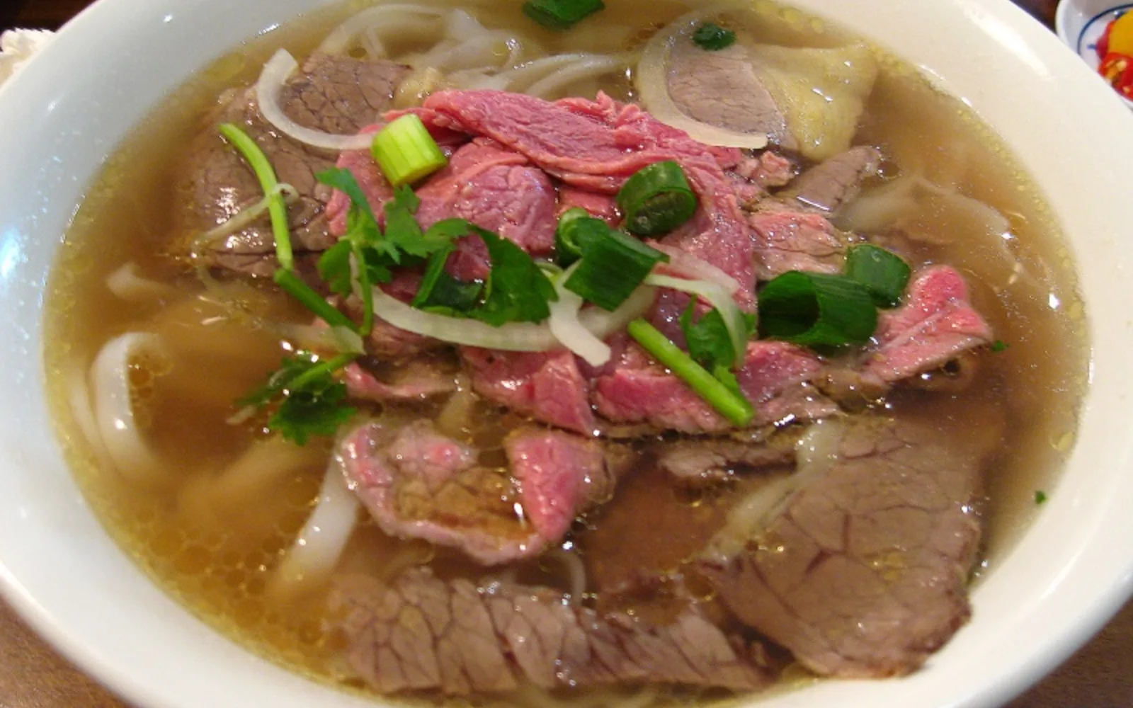 A bowl of Vietnamese phở noodle soup with sliced rare beef and well-done brisket